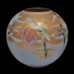 Vaso globular em cerâmica oriental policromada, ornamentado por uma delicada paisagem celeste com várias aves e uma fênix em voo sobre um fundo dourado. Assinado. 22 x 23 cm.