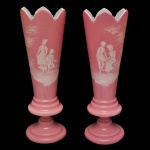 Par de vasos em opalina rosa apresentando corpo cônico com borda superior recortada em formato de bicos. Decoração caracterizado por sua delicada pintura esmaltada branca retratando figuras infantis em ambientes naturais. Base circular pedestalada, dando mais destaque e elegância ao seu design. Apresenta pequeno bicado. 34 x 4 cm.
