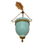 Lanterna de teto de formato cônico alongado, em opalina de cor azul celeste. Bojo liso rematado por pinha na base. Borda levemente revirada e cercada por friso em bronze dourado, ladeado por volutas sustentando correntes reunidas a adorno no formato de sino e canopla no topo. 76 x 32 cm.