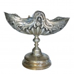 Naveta em prata portuguesa, repuxada e cinzelada, de formato navicular em estilo neoclássico, ornamentada por gomos, folhagens e florões. Bojo oblongo, com parte superior abaulada e elevada ao centro, e tampa reclinável. Haste reta, realçada por bolota, apoiada em base circular almofadada, ornada por guirlanda. Contraste do Porto P Coroa atribuível ao famoso ensaiador José Coelho Sampaio, e marca do prateiro registrado, porém não identificável, datável de 1768-c. 1804 (Moitinho P-16 à p.190 e P-463  à p. 273). 17 x 20 x 8 cm.