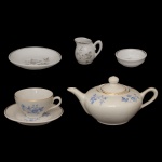 Miniatura de serviço para chá em porcelana  policromada. Apresenta decoração floral em azul e frisos dourados. Constando de 1 bule p/ chá, 1 cremeira, 4 xícaras com seus pires,  manteigueira, bowl p/ geleia. Acondicionadas em estojo original