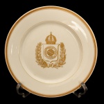 Prato circular em porcelana encomendado para a exposição de 1867 em Paris. Apresenta Brasão de Armas do Brasil em dourado no centro e friso dourado nas bordas. 23 cm. Coleção Ari Bragança de Bourbon.