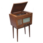 PYE  Antigo móvel vitrola com rádio. Caixa em madeira nobre e clara, com tampo reclinável revelando toca discos. Frente apresentando tela com emissoras de rádio, ladeada por caixa de som. Pernas retas, levemente inclinadas. Apresenta placa com o nome da manufatura inglesa de aparelhos eletrodomésticos, fundada em 1896 e vendida em 1960. 74 x 51 x 34 cm. Não funciona, precisa trocar uma bobina.
