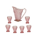 Conjunto de jarra e 6 copos para suco em vidro de cor rosa fosco, decorado com relevos geométricos. Apresenta formato cônico facetado bem característico da estética Art Déco, acompanhado por uma base quadrada e uma alça angular geométrica. Copos acompanhando a mesma decoração. 27 x 25 cm (jarra). 12 cm (copos).