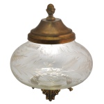 Bomboniere bojuda em vidro translucido e com delicadas lapidações. Tampa em metal dourado com puxador em forma de pinha e base com pés trabalhados. 18 x 17 cm.