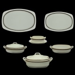 PIAG (First Bohemian Porcelain Manufacturing Company). Tchecoslováquia - Serviço para jantar em porcelana tcheca. Apresenta um design minimalista com superfícies em tom off-white, formato ovalado contemporâneo e um refinado detalhe de frisos duplos em tons de marrom e preto nas bordas. Constando de 28 peças, sendo: 12 pratos rasos (25 cm), 8 pratos fundos (24 cm), 1 sopeira (18 x 38 x 22 cm), 2 legumeiras (12 x 30 x 17 cm / 1 sem tampa / com restauro na alça), 1 molheira (8 x 23 x 15 cm) e 2 travessas (40 x 27 cm / 34 x 23 cm), 2 pratos para arroz (27 cm).