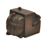 ESCOLA DE EDO. SÉC. XIX - Humorístico netsuke em madeira escura representando o tema clássico de Oni Setsubun. Na festa do Setsubun, no início de fevereiro, os adultos se fantasiam de Demônios Oni e as crianças ficam atirando pequenos bolinhos neles. Nesta peça, um Oni tenta se proteger, escondido dentro de uma caixa.Assinado Masakazu, gravado sobre placa em marfim embutida sob a base. Artista citado com comentários e reproduções de sua assinatura, no livro Netsuke and Inro Artists and How to Read Their Signatures, por George Lazarnick  Reed Publishers  Honolulu 1982, no Volume I nas pag. 707 a 710, o qual menciona igualmente outros manuais com referências ao escultor.
