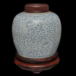 Potiche em porcelana chinesa policromada decorado com azul e branca, sob o vidrado, exibindo padrões florais e ramagens densas (estilo guirlandas florais. Tampa e peanha em madeira. 30 cm (MT). 7 x 24 cm (pote).