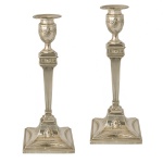 Par de castiçais em prata inglesa repuxada e cinzelada, decorados em estilo neoclássico. Hastes retas em colunas caneladas e afinadas, encimadas por bobeches no formato de vasos com guirlandas e bordas salientes. Bases quadrangulares e almofadadas, ornamentadas por perolados e medalhões. Contrastes de Sheffield com letra data ilegível, porém do início do século XX  e marca do prateiro Thomas A. Scott. 31 x 12 x 12 cm. PESO TOTAL COM ENCHIMENTO 1K.750 gramas. Um castiçal com a parte superior solta.