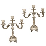 Par de candelabros para 3 velas em prata brasileira, repuxada e cinzelada, decorados com volutas e folhagens. Hastes retas montadas com anelados e elementos de balaústre, ladeadas por braços recurvos, rematados por bobeches no formato de vasos com bordas salientes. Segmentos superiores com pequenos castiçais acompanhando o estilo. Bases cônicas bordadas por frisos lisos e altos, com pés revirados. Contrastes do teor de 833 mls e marcas do fabricante Pratalei. 32 x 27 x 10 cm. Peso total 2K.100 gramas.