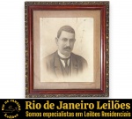 ATELIÊ HUBERT - PORTA-RETRATO DE PAREDE EXECUTADO EM MADEIRA NOBRE COM MOLDURA DUPLA DE ÉPOCA, SEÇÃO EXTERNA APRESENTA RICO TRABALHO EM RELEVO ORNAMENTADO COM DOURAÇÃO FLORAL E SEÇÃO INTERNA EXIBE ACABAMENTO EM MADEIRA COM PASSE-PARTOUT INTEGRADO ORIGINAL EM CARTÃO E VIDRO, ACOMPANHADO DE FOTOPINTURA (FOTOGRAFIA ANTIGA DE ÉPOCA COM INTERVENÇÃO ARTÍSTICA MANUAL/RETOQUES A GRAFITE OU CARVÃO) RETRATANDO FIGURA MASCULINA COM TRAJES FORMAIS (PALETÓ, COLETE E GRAVATA) E BIGODE , MEDINDO 63 X 56 CM. APRESENTA MARCAS DO TEMPO, USO, DESGASTES NA MADEIRA, MARCAS E MANCHAS DE OXIDAÇÃO/UMIDADE NO PASSE-PARTOUT E NA IMAGEM COMPATÍVEIS COM SUA ANTIGUIDADE E ESTADO DE CONSERVAÇÃO, CONFORME FOTOS EXTRAS. ESCLAREÇA TODAS AS DÚVIDAS ANTES DE EFETUAR SEU LANCE, QUE SERÁ CONSIDERADO IRREVOGÁVEL E IRRETRATÁVEL. CONSULTE PREVIAMENTE OS TERMOS E CONDIÇÕES DISPONÍVEIS NO SITE. CONTATO (21) 98264-3000.