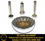 CONJUNTO, PARTE DE SERVIÇO DE MESA, EXECUTADO EM METAL ESPESSURADO À PRATA COMPOSTO POR QUATRO PEÇAS, SENDO: DOIS CASTIÇAIS, , BASE CIRCULAR E CORPO CILÍNDRICO AFUNILADO, MEDINDO 16 CM CADA; PALITEIRO, CORPO CILÍNDRICO ALONGADO E VERTICAL, ASSENTADO SOBRE UMA BASE CIRCULAR ROBUSTA COM MOLDURAS ESCALONADAS EM RELEVO, APRESENTA TAMPA CIRCULAR PLANA, PINO ROSQUEADO SALIENTE PARA ACIONAR O MECANISMO DE ELEVAÇÃO DOS PALITOS, MEDINDO 14 CM E UVEIRA, BORDA RENDADA COM DELICADOS DETALHES VAZADOS EM PADRÃO FLORAL, ALÇA MÓVEL, MEDINDO 15,5 X 20 CM. APRESENTAM MARCAS DO TEMPO, USO, DESGASTES E/OU IMPERFEIÇÕES COMPATÍVEIS COM SUA UTILIZAÇÃO E ESTADO DE CONSERVAÇÃO, DESTACANDO PERDA NO BANHO, CONFORME FOTOS EXTRAS. ESCLAREÇA TODAS AS DÚVIDAS ANTES DE EFETUAR SEU LANCE, QUE SERÁ CONSIDERADO IRREVOGÁVEL E IRRETRATÁVEL. CONSULTE PREVIAMENTE OS TERMOS E CONDIÇÕES DISPONÍVEIS NO SITE. CONTATO VIA TELEFONE OU WHATSAPP: (21) 98264-3000.