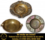 CONJUNTO DE CINZEIROS EXECUTADO EM METAL DOURADO, POSSIVELMENTE BRONZE, COMPOSTO POR TRÊS PEÇAS, SENDO:  UM, COM FORMATO CIRCULAR, DUAS PEQUENAS ALÇAS LATERAIS INTEGRADAS AO CORPO DA PEÇA, ACABAMENTO COM FRISOS VERTICAIS EM RELEVO NA PARTE EXTERNA, MEDINDO 16,5 CM; UM, COM FORMATO QUADRILOBADO, RICA ORNAMENTAÇÃO EM ALTO-RELEVO INSPIRADA EM MOTIVOS FLORAIS E ARABESCOS, CENTRO APRESENTA MEDALHÃO DECORATIVO EM RELEVO, MEDINDO 12,5 X 14,5 CM E UM, DECORADO COM PINTURA ESMALTADA, CENTRO APRESENTA RICA GRAVURA EM RELEVO COM FIGURA DE PAVÃO CERCADO POR ELEMENTOS ORNAMENTAIS, BORDA É DECORADA COM MOTIVOS FLORAIS E ARABESCOS INSPIRADOS NA ARTE ORIENTAL, APRESENTA QUATRO APOIOS PARA CIGARRO DISTRIBUÍDOS AO REDOR DA BORDA, MEDINDO 13 CM. APRESENTAM MARCAS DO TEMPO, USO, DESGASTES E/OU IMPERFEIÇÕES COMPATÍVEIS COM SUA UTILIZAÇÃO E ESTADO DE CONSERVAÇÃO, CONFORME FOTOS EXTRAS. ESCLAREÇA TODAS AS DÚVIDAS ANTES DE EFETUAR SEU LANCE, QUE SERÁ CONSIDERADO IRREVOGÁVEL E IRRETRATÁVEL. CONSULTE PREVIAMENTE OS TERMOS E CONDIÇÕES DISPONÍVEIS NO SITE. CONTATO VIA TELEFONE OU WHATSAPP: (21) 98264-3000.