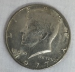 Moeda norte-americana de Half Dollar (50Cents), ano 1977, com retrato do presidente John F. Kennedy no anverso. Peça em metal de composição cobre-níquel, com sinais de circulação e do tempo.