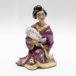 Escultura em porcelana representando gueixa. Leque se encontra colado. Altura: 22cm.