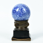 Bola em porcelana chinesa, com pedestal em bronze sobre base de madeira. Altura total: 19,5cm; Diâmetro: 10cm.