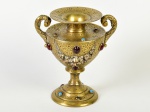 Ânfora em bronze dourado, ricamente cinzelada com motivos florais e aplicação de pedrarias. Parte superior apresenta leve afundamento. Altura: 21cm.