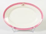 CH. PILLIVUYT - Travessa em porcelana francesa esmaltada e vitrificada na cor branca, bordas decoradas com faixa rosa, fio dourado e monograma. Apresenta bicado na borda. Medidas: 5 x 49,5 x 27,5cm.