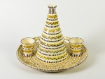 LUIZ SALVADOR - Conjunto de prato (31cm diâmetro), garrafa (22,5cm de altura) e 2 copos (6,5cm de altura), em cerâmica esmaltada e vitrificada na tonalidade creme, com decorações nos tons marrom, amarelo, vermelho e verde. Copos apresentam leves bicados na base.