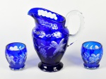 Conjunto de jarro e 2 copos em cristal double na cor azul, decorados com lapidação floral. Jarra apresenta trincado. Altura da jarra: 19,5cm; Copos: 8cm.