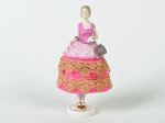 Boneca em porcelana esmaltada e vitrificada, saia em tecido na cor rosa. Altura: 18cm.