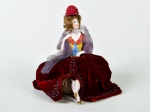 Boneca em porcelana alemã, representando dama sentada, saia em tecido na cor vinho. Altura: 17cm.