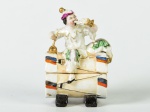 Pequena caixa porta joias em porcelana, decorada com escultura de pierrot. Escultura apresenta pé quebrado. Medidas: 12 x 8,5 x 6cm.