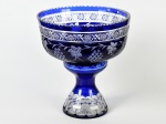 Grande centro de mesa em vidro doublé na cor azul, base desmontável, decorado com lapidações em frutos, gomos e estrelas. Apresenta bicados na borda. Altura total e diâmetro: 33 x 30cm.