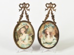Par de antigos pequenos quadros, moldura em metal dourado, suporte cinzelado com motivos florais e laço. Medidas da moldura: 12,5 x 9,5cm; Altura total: 20,5cm.