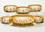 LUIZ XV - Conjunto de rocamboleira e 5 bandejas em porcelana esmaltada e vitrificada dourada, decoradas com cenas galantes. Algumas peças apresentam leve desgaste na coloração. Medidas: 3 x 34,5 x 16cm / 2 x 20 x 11cm.