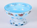 Fruteira em cristal overlay, nas cores branco opalinado e azul, decorada com motivos florais e lapidação em gomos. Apresenta discretos bicados na borda. Altura e diâmetro: 11,5cm.