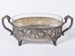 Centro de mesa art noveau em metal espessurado a prata, cinzelado com motivos florais, recipiente em vidro translúcido. Medidas: 16 x 40 x 16cm.