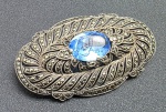 BROCHE - Antigo broche oval em prata adornado com marcassitas e pedra azul no centro. Medidas: 6 x 3 cm. Alfinete amassado.