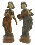 Par de esculturas em madeira nobre policromada, representando figuras femininas em trajes de época tocando instrumentos musicais; apoiadas em bases octogonais. Medidas: 38 x 10 cm. Pintura com ínfimos desgastes.