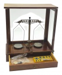 MARTE  - BALANÇA DE PRECISÃO - Antiga balança de precisão da marca Marte, tradicionalmente utilizada em farmácias e laboratórios ou por ourives em meados do século XX. Tem uma estrutura de base e gabinete em madeira com feixes de vidro protetores para evitar interferências de correntes de ar na pesagem. A balança é do tipo analógica com dois pratos suspensos com haste central e fiel de medida. Medida: 44cm x 41cm. Possui pequeno estojo com alguns pesos. Observação; Não testada, pesos com pequenos pontos de oxidação. Contém ínfimas marcas e desgastes.