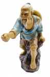 Escultura representando um pescador, em trajes típicos orientais. Fabricada na China, em cerâmica esmaltada multicolorida. Medidas: 19 x 15 cm. Vara de pesca ausente.