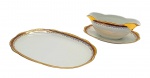 PORCELANA RENNER, PORTO ALEGRE - Parte de serviço de jantar com 01 molheira com presentoir integrado e 01 travessa oval, decoradas com faixas na cor vinho, e arabescos e motivos vegetalistas em dourado. Em porcelana. Medidas: 22 x 19 cm; 29 x 20 cm.
