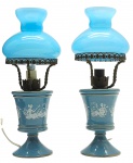 Par de antigas luminárias de mesa com cúpulas em vidro opalinado azul, seção central adornada com cena galante clássica em branco e base tipo pedestal; seção central e base pedestal em porcelana azul com filetes dourados. Fabricação italiana. Medidas: 29 x 11 cm. Não testadas. Metal escurecido.