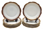 PORCELANA RENNER, PORTO ALEGRE - Parte de serviço de jantar com 12 pratos de sobremesa decorados com faixa na cor vinho, e arabescos e motivos vegetalistas em dourado. Em porcelana. Medidas: 17 cm (diâm.).