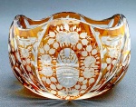 Cachepot oval em cristal double na cor âmbar, lapidado com bordas onduladas, elementos florais e geométricos. Medidas: 15 x 10 cm.