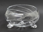 Centro de mesa redondo em robusto cristal translúcido, lapidado com caneluras e padrões fitomórficos no fundo; base trípode no formato de volutas. Medidas: 23 x 13 cm.