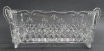 Cachepot retangular em cristal translúcido, com borda adornada com volutas e alças laterais; decorado com padrões fitomórficos e geométricos; apoiado sobre duas bases curvas. Medidas: 31 x 13 x 11 cm.