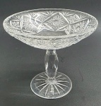 Centro de mesa em cristal translúcido lapidado com padrões fitomórficos e estelares; base pedestal sendo a haste com detalhes ovais. Medidas: 20,5 x 18,5 cm.