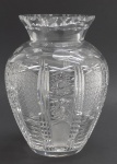 Vaso em cristal translúcido com borda no formato de gola e corpo ovalado, lapidado com padrões fitomórficos, estelares e caneluras verticais. Medidas: 26 x 19 cm. Ínfimos bicados na borda.