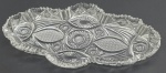 Travessa em cristal translúcido, no formato oval com recortes ondulados e borda serrilhada; lapidada com padrões fitomórficos, estelares e geométricos. Medidas: 39 x 21 cm.