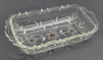 Travessa retangular em cristal translúcido, com borda ondulada moldada com volutas; corpo lapidado com motivos florais com detalhes em vermelho e motivos vegetalistas. Medidas: 30 x 17 cm.