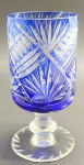 Vaso cilíndrico em cristal double azul, com base pedestal em cristal incolor; corpo lapidado com padrões fitomórficos, caneluras e elementos ovais. Medidas: 20,5 x 10 cm. Ínfimos bicados na borda.