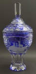 Magnífico potiche em robusto cristal double na cor azul cobalto, com pega da tampa facetada; tampa e corpo lapidados com elementos ovais, sendo a tampa com um medalhão com pássaro e o corpo com um medalhão com casal de cervos, ambos num cenário campestre. Base no estilo pedestal. Medidas: 48 x 22 cm.