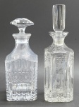 02 diferentes licoreiras em cristal translúcido, sendo uma com tampa hexagonal e facetada, e a outra com tampa cilíndrica com caneluras; corpo retangular com diferentes padrões decorativos que incluem elementos ovais, geométricos e estelares. Medidas: 29 x 9 cm; 26 x 10 cm. Tampas com ínfimo bicado na base.