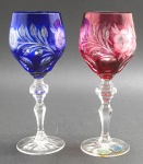 BEYER BLEIKRISTALL, GERMANY - 02 taças em cristal double nas cores azul cobalto e cereja, lapidadas com elementos florais, vegetalistas e ovais; pé alto com haste multifacetada; cristal com 24% de óxido de chumbo, apreciado por sua clareza brilhante. Fabricação alemã. Medidas: 20 x 8 cm. Taça azul cobalto com ínfimo bicado na borda.